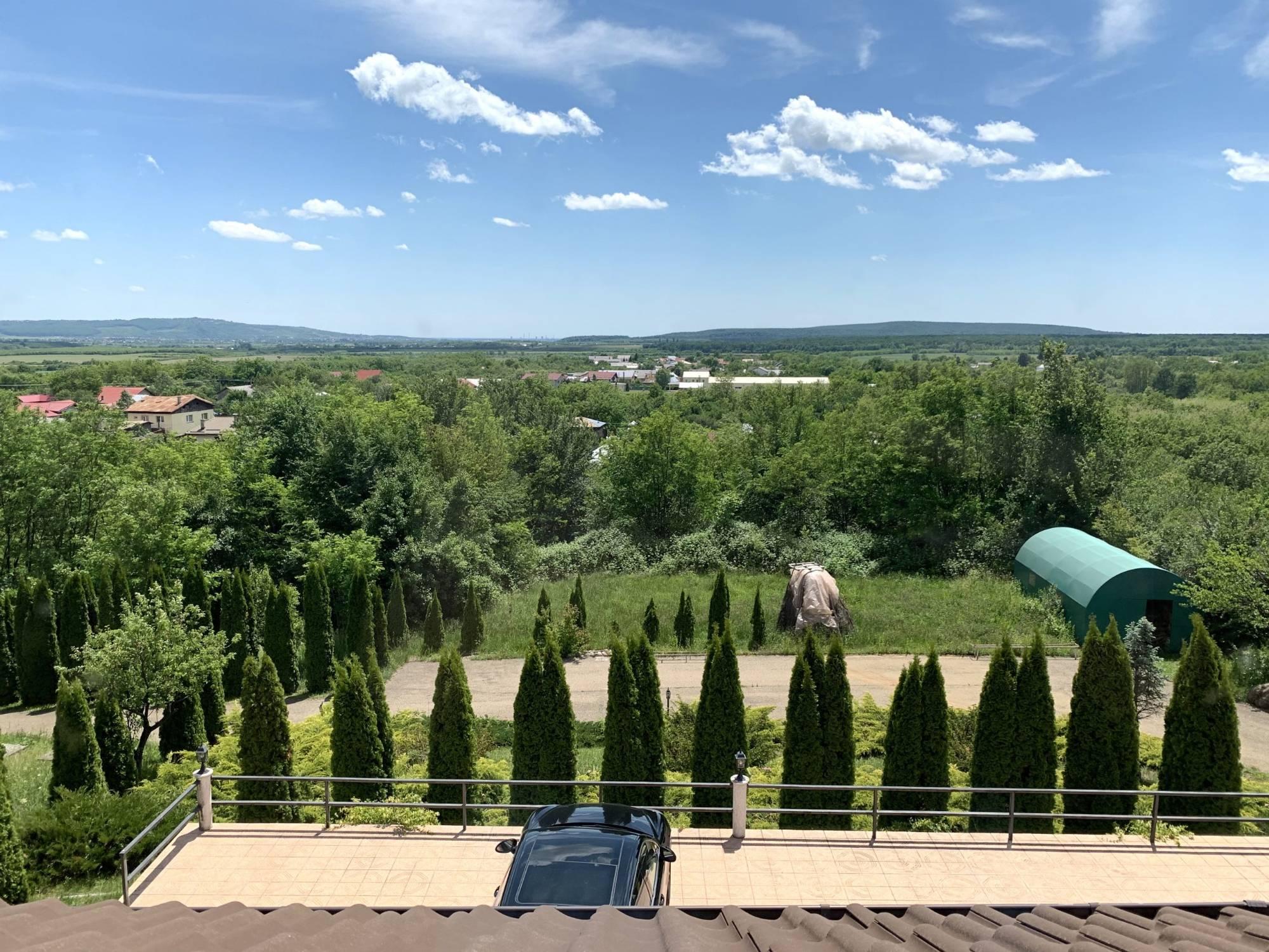 Panorama deschisă de pe terasa Hidden Hills, peste pădure, spre satul din vale și dealurile din zare